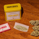 Mom Grass CBG Hemp Flower Half Ounce In A Yellow Tin On A Wooden table
