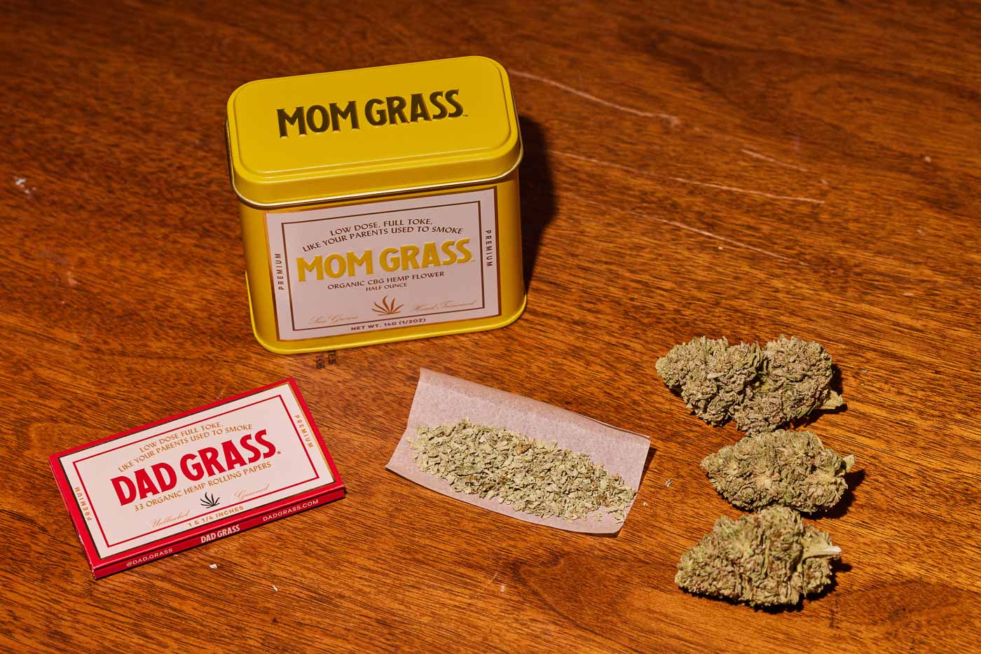 Mom Grass CBG Hemp Flower Half Ounce In A Yellow Tin On A Wooden table