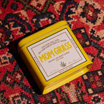 Mom Grass CBG Hemp Flower Half Ounce In A Yellow Tin On A Red Cloth