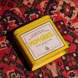 Mom Grass CBG Hemp Flower Half Ounce In A Yellow Tin On A Red Cloth