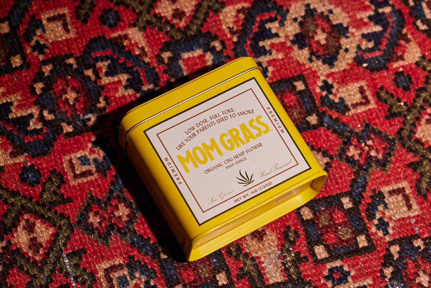 Mom Grass CBG Hemp Flower Half Ounce In A Yellow Tin On A Red Cloth