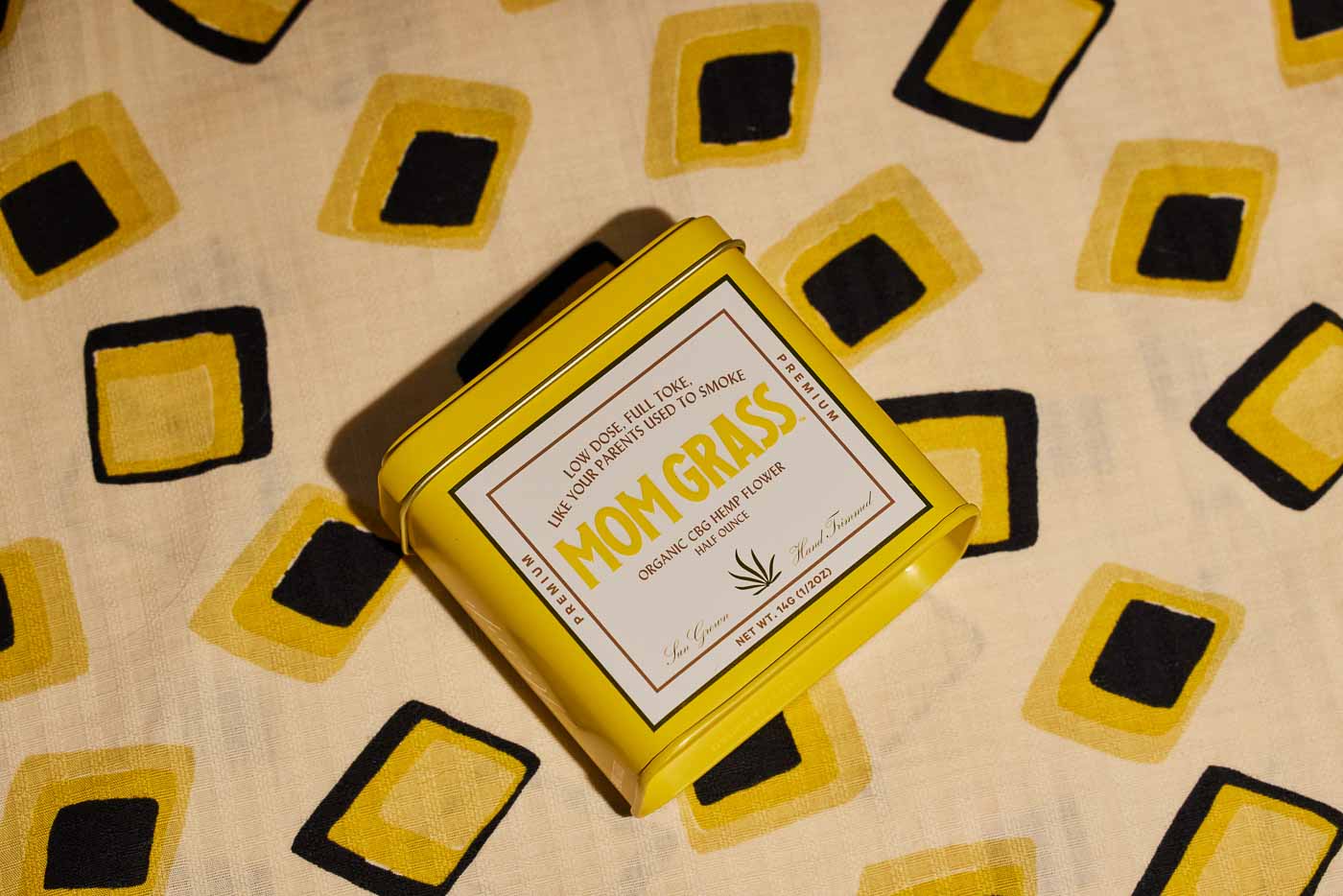 Yellow Mom Grass CBG Hemp Flower Tin On A Yellow Cloth