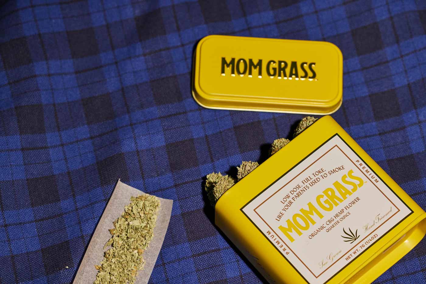 Crushed CBG On A Rollin Paper With A Yellow Mom Grass CBG Hemp Flower Tin On A Blue Cloth