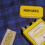 Crushed CBG On A Rollin Paper With A Yellow Mom Grass CBG Hemp Flower Tin On A Blue Cloth