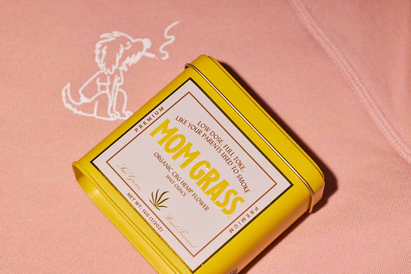 Mom Grass CBG Hemp Flower Half Ounce In A Yellow Tin On A Rollie Hoodie
