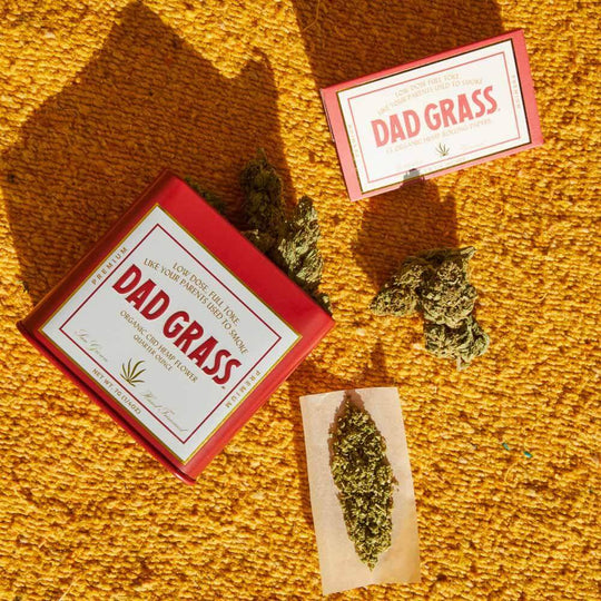 CBD Flower on a rolling paper and Red Dad Grass Tin on an Orange rug