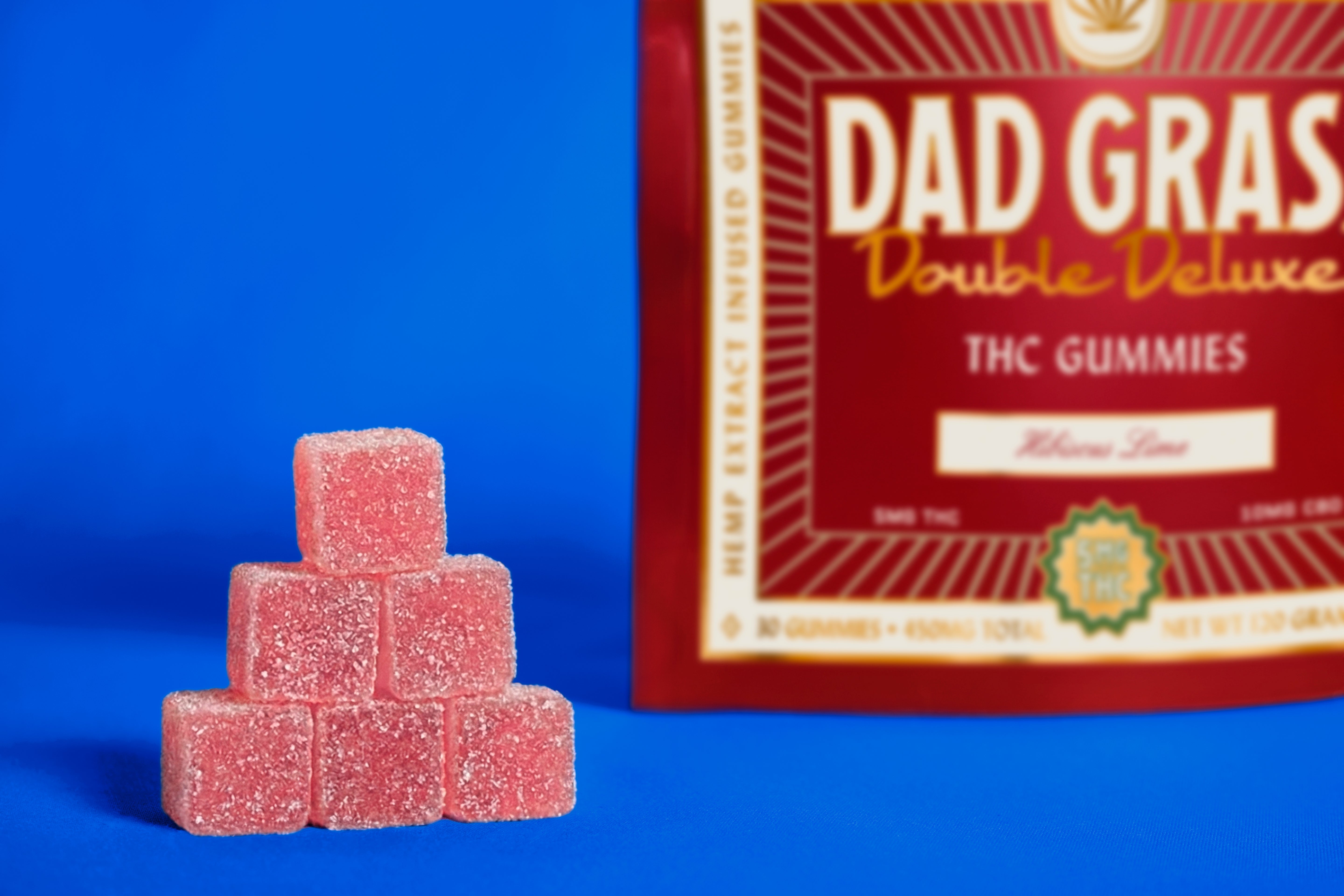 Stack of red THC gummies in front of a 'Dad Gras' packaging on a blue background
