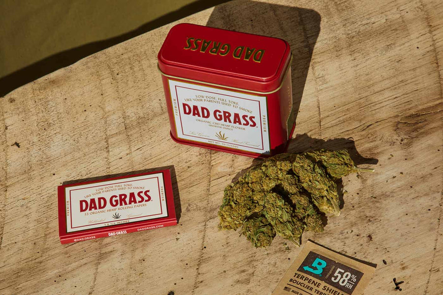 Dad Grass CBD Hemp Flower In A Red And On The Table With Rolling Papers Top View